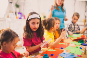 The group of children are sitting at a table and making an applique of colored paper